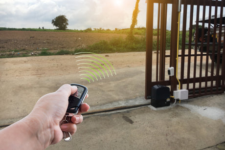 Someone controlling an automatic security gate with a remote. Green signal rays spread from the remote to the gate.
