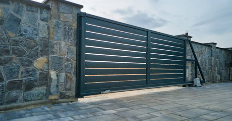 An elegant and efficient automatic gate opener system set into a beautiful stone wall. The sky is cloudy overhead.