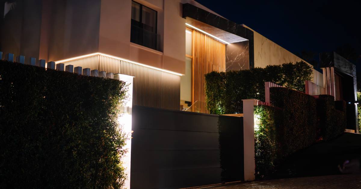 An elegant home protected by a visually appealing automatic gate. It's late at night and the lights are on.
